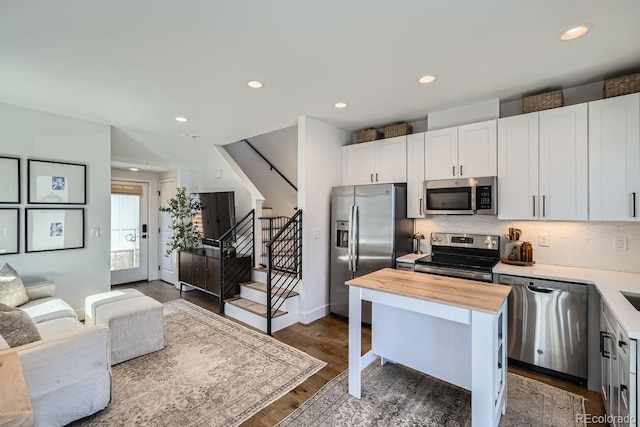 kitchen with white cabinets, decorative backsplash, dark wood finished floors, butcher block counters, and stainless steel appliances