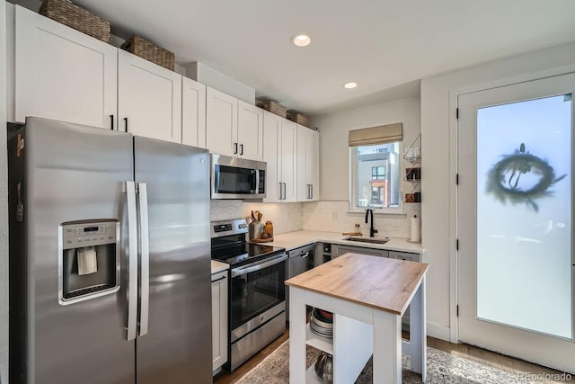 kitchen featuring white cabinets, decorative backsplash, butcher block countertops, appliances with stainless steel finishes, and a sink