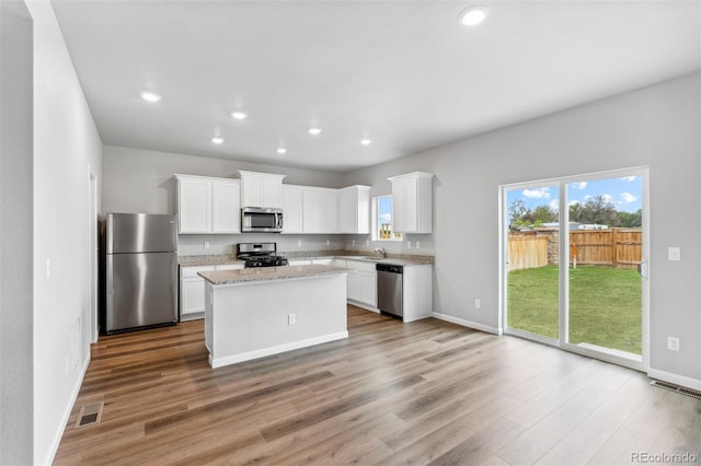 kitchen with appliances with stainless steel finishes, a kitchen island, white cabinetry, sink, and light stone counters