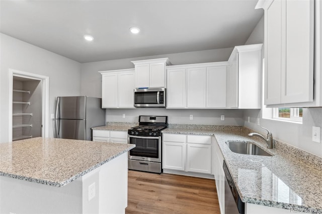 kitchen featuring white cabinets, stainless steel appliances, sink, light wood-type flooring, and light stone counters