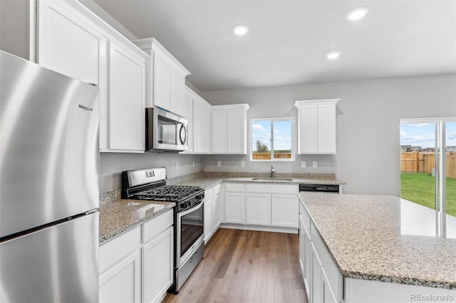 kitchen featuring appliances with stainless steel finishes, white cabinetry, light hardwood / wood-style floors, sink, and light stone counters