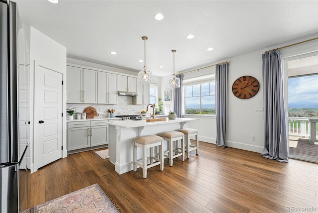 1601 Mariah Ln, Erie, CO 80516 - kitchen featuring under cabinet range hood, light countertops, dark wood-type flooring, baseboards, and a breakfast bar area