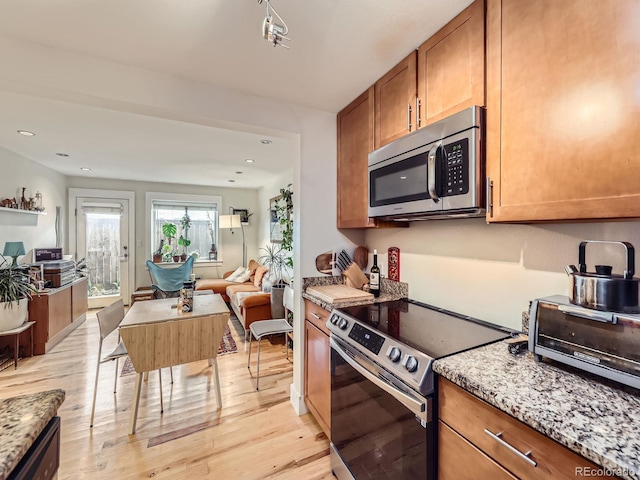 2460 W Caithness Pl Unit 105, Denver, CO 80211 - kitchen featuring appliances with stainless steel finishes, open floor plan, light wood-style floors, brown cabinetry, and light stone countertops