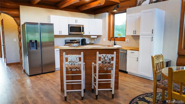 kitchen with wooden counters, white cabinets, beamed ceiling, appliances with stainless steel finishes, and light wood finished floors