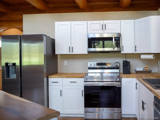 kitchen featuring white cabinetry, butcher block counters, stainless steel appliances, beam ceiling, and sink