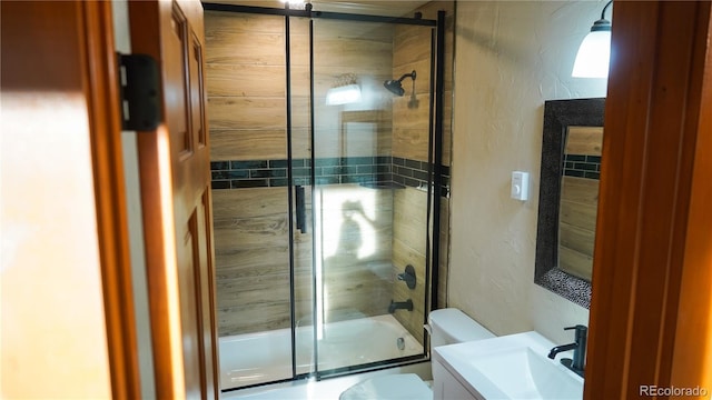 bathroom featuring toilet, enclosed tub / shower combo, vanity, and a textured wall