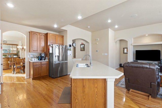 kitchen with light hardwood / wood-style flooring, sink, stainless steel fridge, and an island with sink