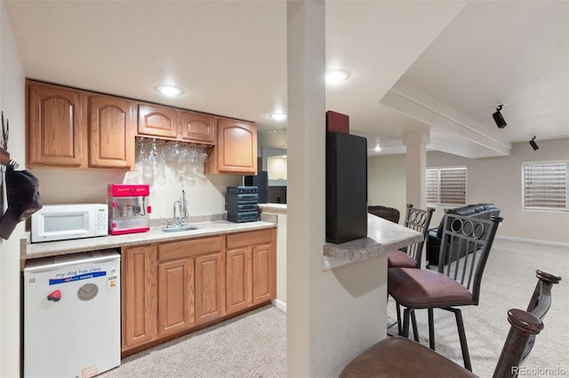 kitchen with sink, light colored carpet, a kitchen breakfast bar, and refrigerator