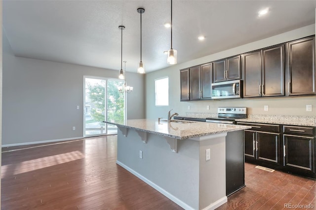 15955 E Otero Cir, Centennial, CO 80112 - kitchen with appliances with stainless steel finishes, light stone countertops, dark wood finished floors, a kitchen island with sink, and a breakfast bar