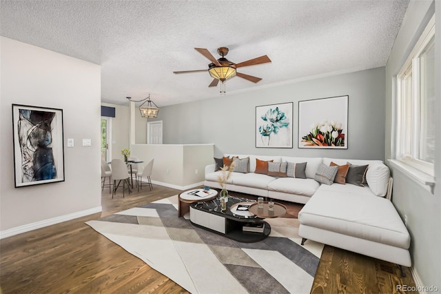 living room with ceiling fan with notable chandelier, wood-type flooring, and a textured ceiling