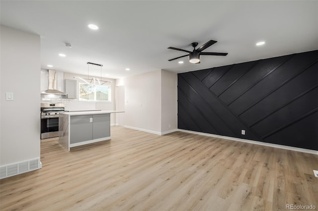 kitchen featuring a kitchen island, stainless steel range, white cabinetry, wall chimney range hood, and hanging light fixtures