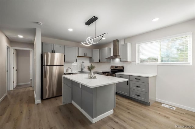 kitchen with appliances with stainless steel finishes, hanging light fixtures, wall chimney range hood, a kitchen island, and sink