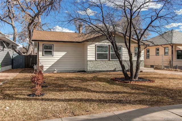 view of front of property featuring stone siding, fence, and a front yard