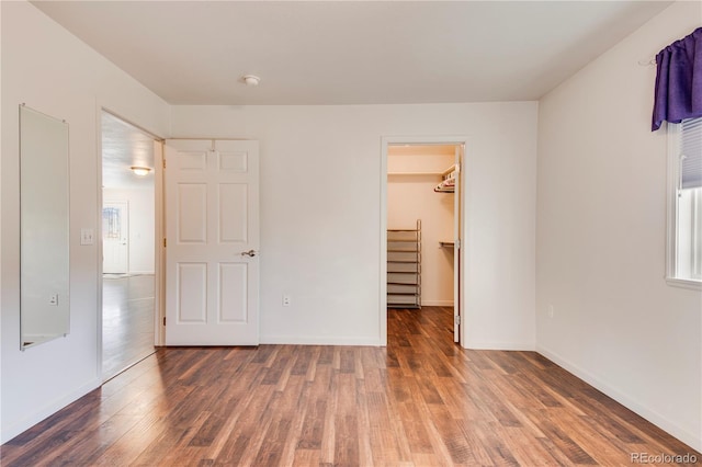 unfurnished bedroom with a spacious closet, dark wood-type flooring, and a closet