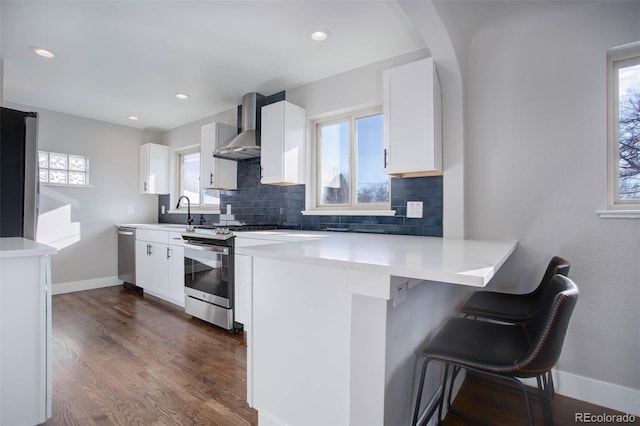 kitchen with a wealth of natural light, white cabinetry, stainless steel appliances, wall chimney range hood, and a breakfast bar area