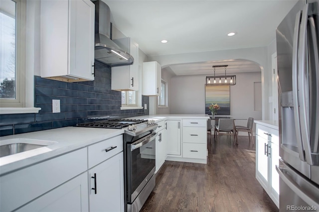 kitchen featuring white cabinets, wall chimney exhaust hood, hanging light fixtures, and appliances with stainless steel finishes