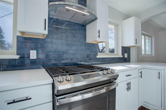 kitchen featuring gas stove, backsplash, white cabinetry, and ventilation hood