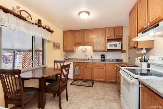 kitchen featuring brown cabinets, under cabinet range hood, a sink, backsplash, and white appliances