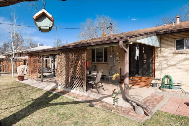 back of property featuring brick siding, fence, entry steps, a lawn, and a patio