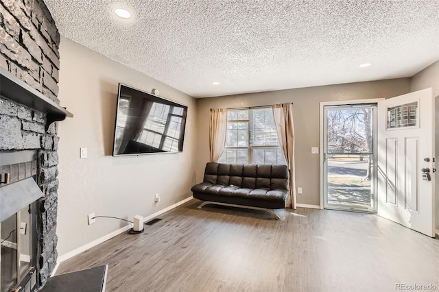 unfurnished room with visible vents, baseboards, a stone fireplace, and wood finished floors