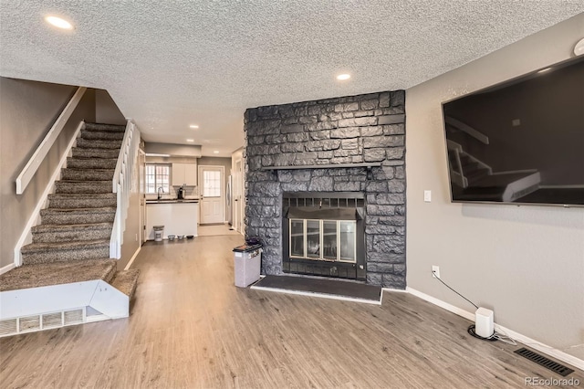 unfurnished living room featuring visible vents, a textured ceiling, wood finished floors, a stone fireplace, and baseboards