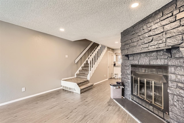 unfurnished living room featuring a stone fireplace, stairs, wood finished floors, and baseboards