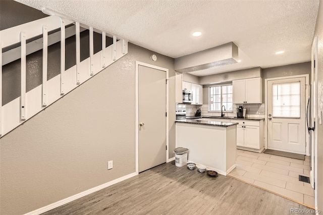 kitchen with dark countertops, backsplash, light wood-style flooring, white cabinetry, and a sink