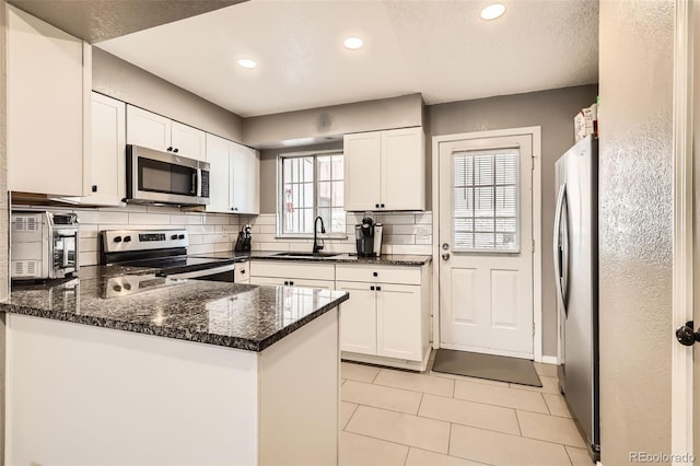 kitchen with decorative backsplash, a peninsula, stainless steel appliances, white cabinetry, and a sink