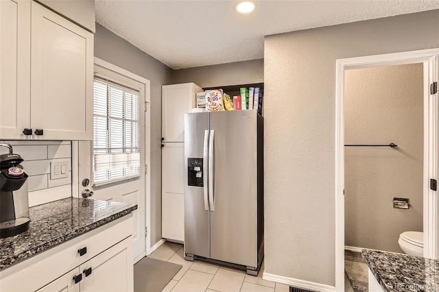 kitchen featuring baseboards, dark stone counters, light tile patterned flooring, white cabinets, and stainless steel fridge