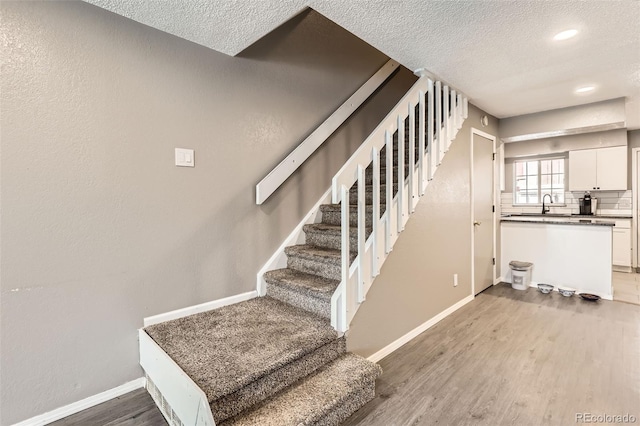 staircase with a textured ceiling, baseboards, and wood finished floors