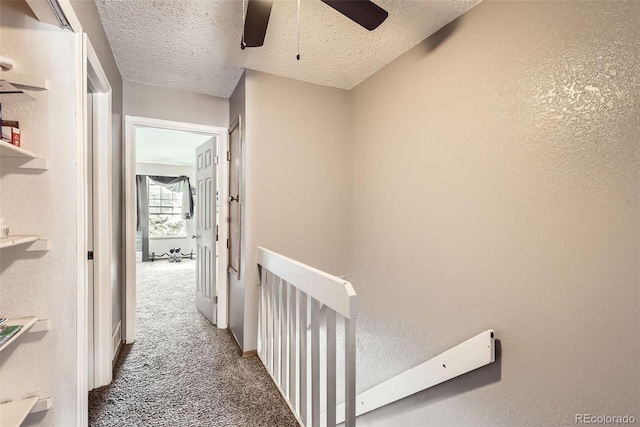 corridor featuring an upstairs landing, carpet, a textured wall, and a textured ceiling