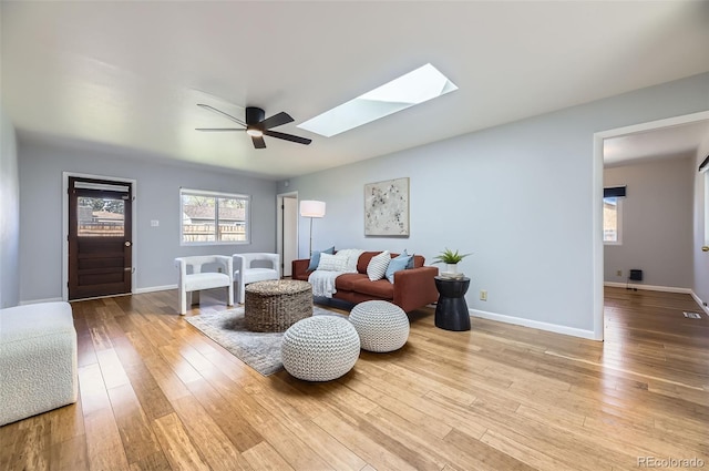 living area with ceiling fan, a skylight, wood-type flooring, and baseboards