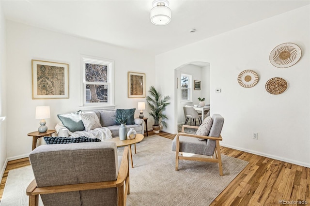 living room featuring arched walkways, light wood finished floors, and baseboards