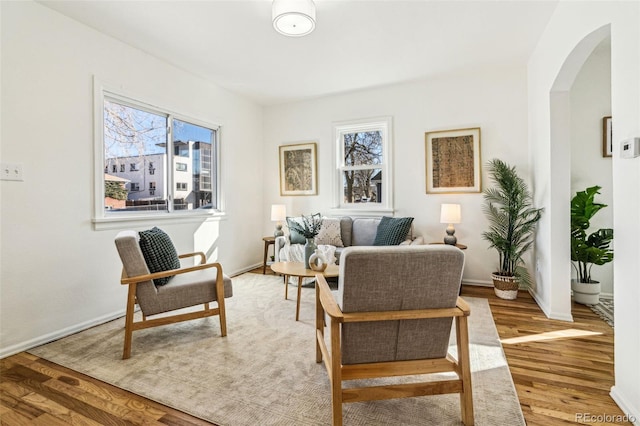 sitting room featuring arched walkways, light wood-type flooring, and baseboards