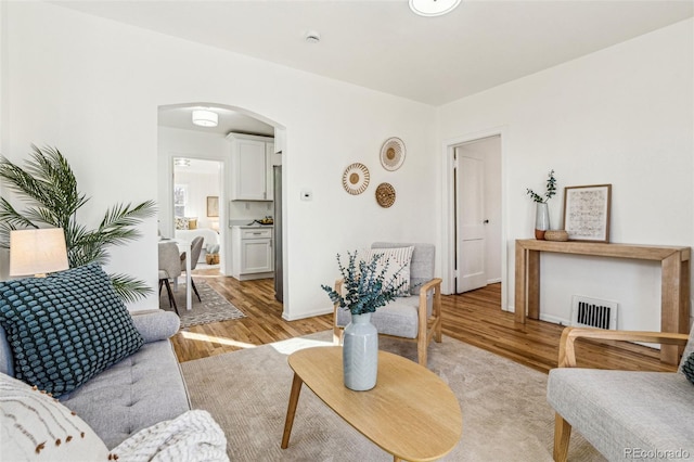 living room with light wood-type flooring, arched walkways, visible vents, and baseboards