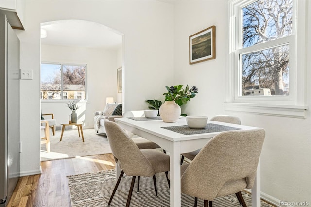 dining space with light wood-style flooring, arched walkways, and baseboards