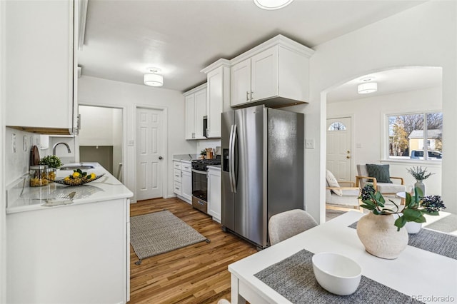 kitchen with arched walkways, white cabinets, appliances with stainless steel finishes, light countertops, and a sink