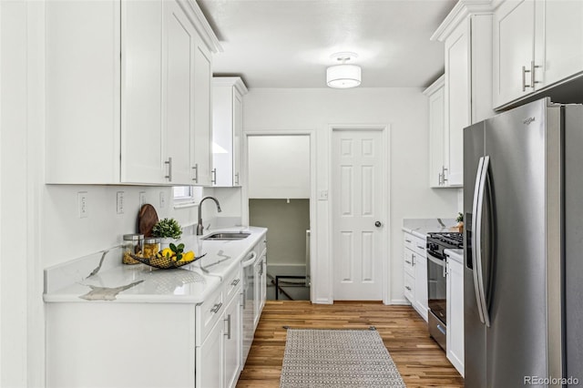 kitchen featuring appliances with stainless steel finishes, white cabinets, a sink, and wood finished floors