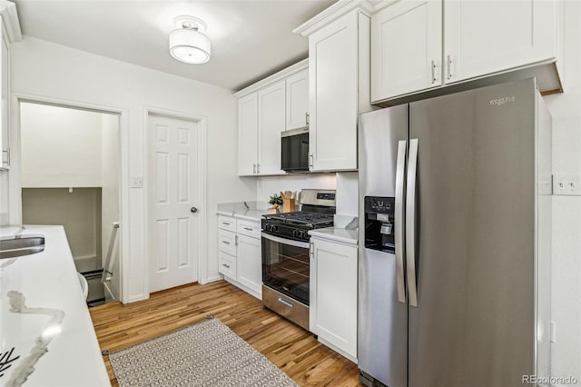 kitchen with light stone counters, a sink, white cabinetry, light wood-style floors, and appliances with stainless steel finishes