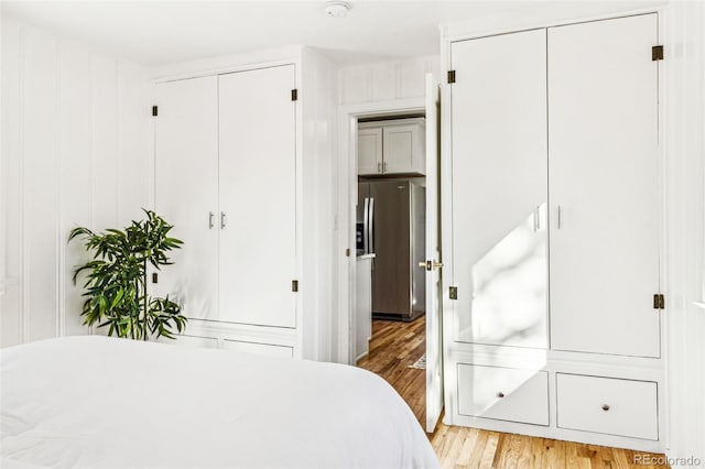 bedroom with light wood-style floors, stainless steel refrigerator with ice dispenser, and multiple closets