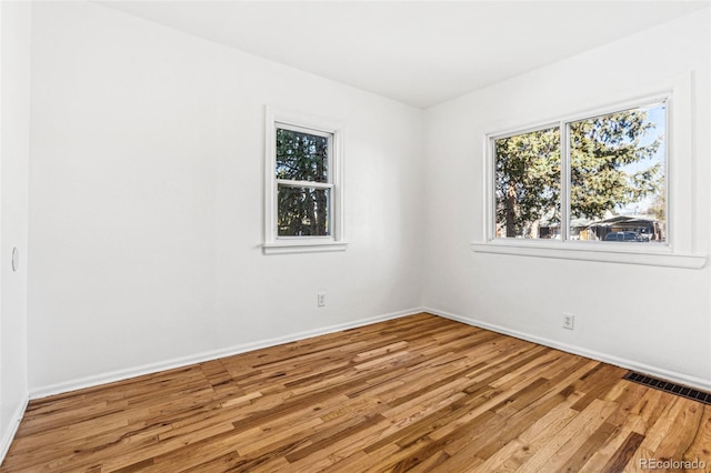 spare room with baseboards, plenty of natural light, visible vents, and wood finished floors