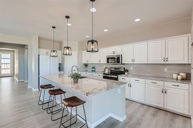 711 N Waterloo Ct, Aurora, CO 80018 - kitchen with stainless steel appliances, a sink, light wood-type flooring, white cabinets, and a breakfast bar
