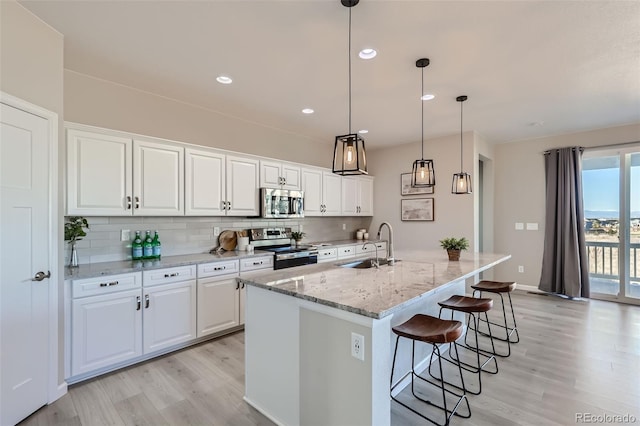 kitchen with stainless steel appliances, white cabinetry, a kitchen island with sink, and light stone counters