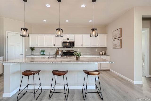 kitchen with light wood-type flooring, white cabinetry, appliances with stainless steel finishes, light stone countertops, and a kitchen island with sink