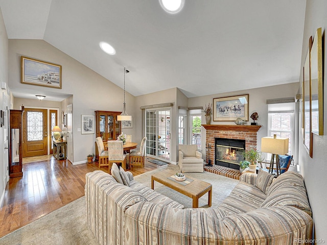 living area featuring wood-type flooring, a brick fireplace, plenty of natural light, and baseboards