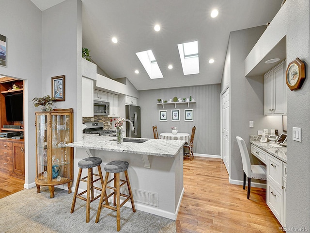 kitchen with appliances with stainless steel finishes, light stone counters, light wood finished floors, a breakfast bar area, and a peninsula