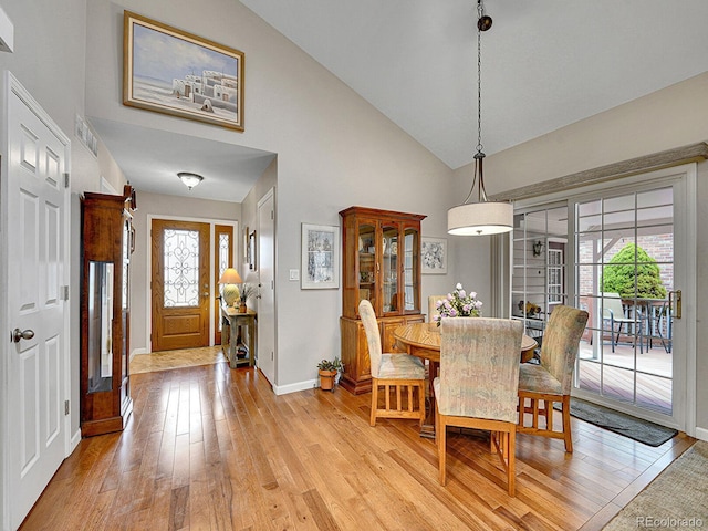 dining area with baseboards, light wood finished floors, a healthy amount of sunlight, and high vaulted ceiling