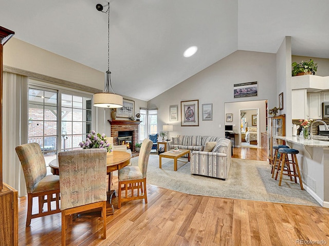 dining area featuring light wood-style floors, high vaulted ceiling, and a fireplace