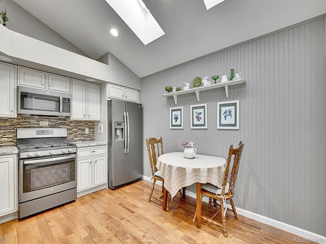 kitchen featuring light wood-style floors, stainless steel appliances, white cabinetry, decorative backsplash, and lofted ceiling with skylight
