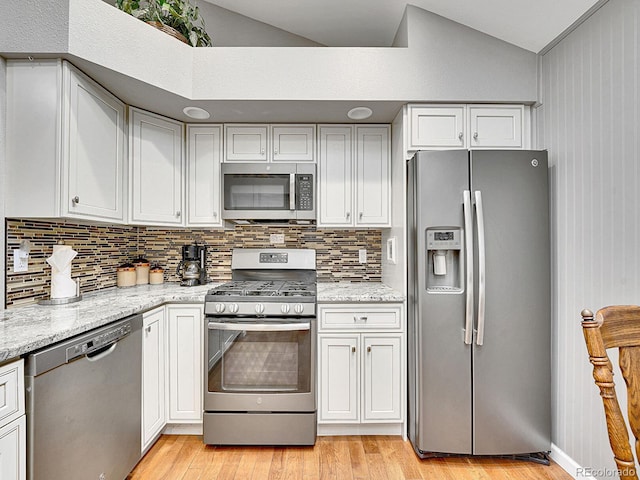 kitchen featuring stainless steel appliances, vaulted ceiling, light wood-style flooring, and tasteful backsplash